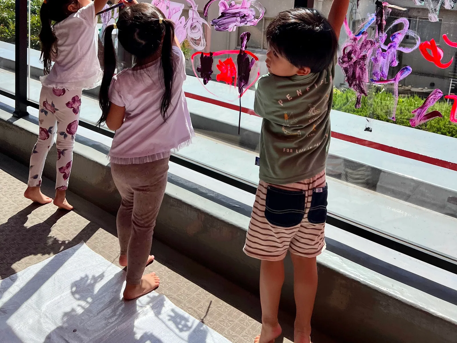 屋上のガラスに絵の具でお絵かきする園児たち（後ろ姿）